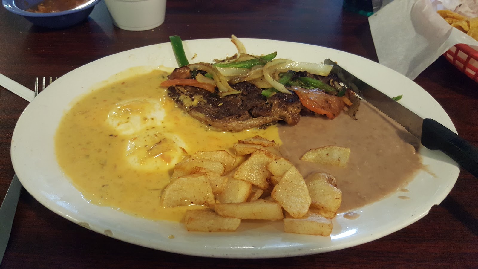 Grilled steak plate with eggs, fried potatoes and refried beans