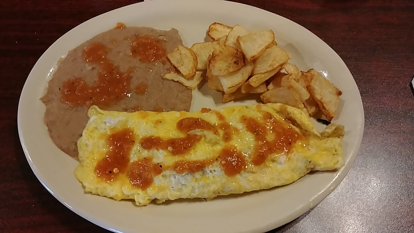 Egg plate topped with hot sauce alongside refried beans and fried potatoes