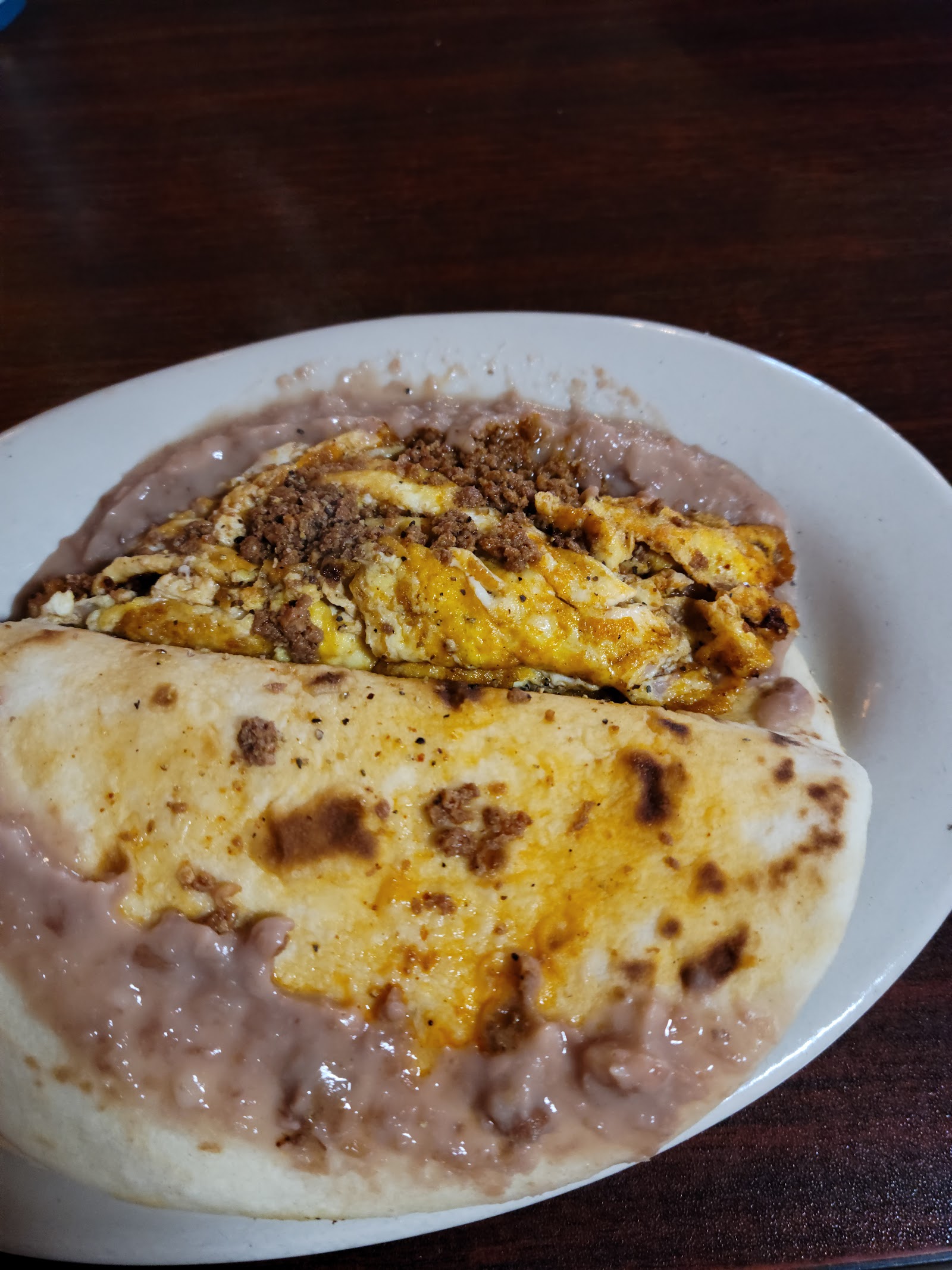 Breakfast taco with egg, cheese and ground beef next to refried beans